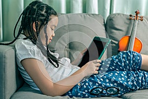 Cute little girl,playing with computer at home laying on sofa