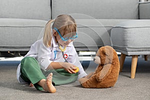 A cute little girl is playing in a doctor costume with a teddy bear. A happy child is playing at the hospital.