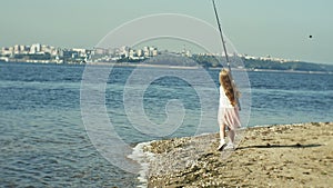 Cute little girl is playing with a fishing rod on a fishing boat near the river