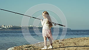 Cute little girl is playing with a fishing rod on a fishing boat near the river