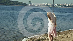 Cute little girl is playing with a fishing rod on a fishing boat near the river