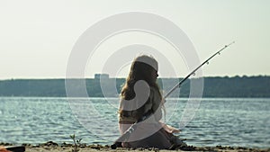 Cute little girl is playing with a fishing rod on a fishing boat near the river