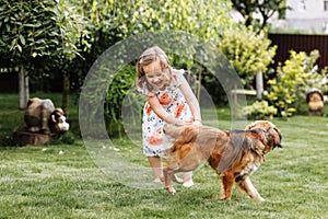 A cute little girl is playing with her pet dog outdooors on grass at home