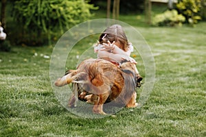 A cute little girl is playing with her pet dog outdooors on grass at home