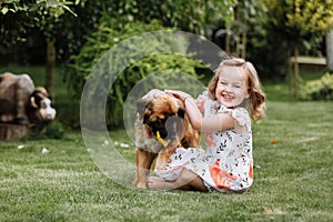 A cute little girl is playing with her pet dog outdooors on grass at home