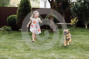 A cute little girl is playing with her pet dog outdooors on grass at home