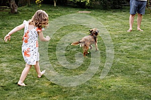 A cute little girl is playing with her pet dog outdooors on grass at home