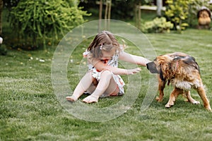 A cute little girl is playing with her pet dog outdooors on grass at home