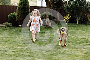 A cute little girl is playing with her pet dog outdooors on grass at home. selective focus
