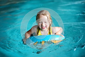Cute little girl playing with inflatable ring in indoor pool. Child learning to swim. Kid having fun with water toys.