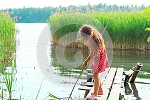 Cute Little girl is playing and looking at the lake at summer day.Place for text