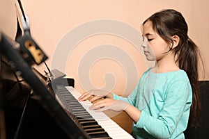 Cute little girl playing piano near wall. Music lesson