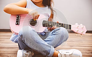 Cute little girl playing pink ukulele sitting on floor photo