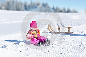 Cute little girl playing in the snow. Sled in background