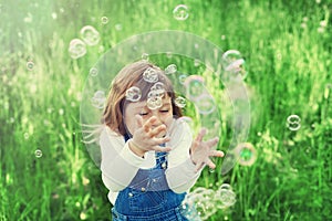 Cute little girl playing with soap bubbles on the green lawn outdoor, happy childhood concept, child having fun