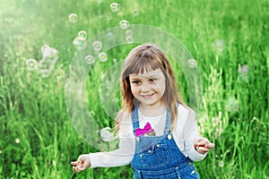 Cute little girl playing with soap bubbles on the green lawn outdoor, happy childhood concept, child having fun