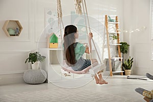 Cute little girl playing on swing at home