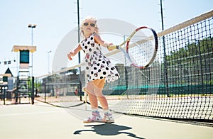 Cute little girl playing tennis on the tennis court outside