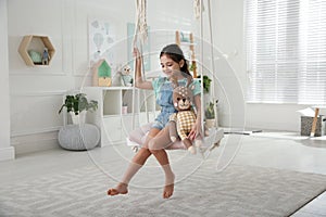 Cute little girl playing with toy deer on swing at home