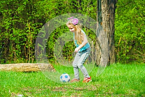 A cute little girl plays with a ball on a green meadow.