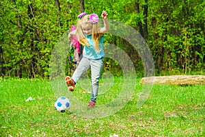 A cute little girl plays with a ball on a green meadow.