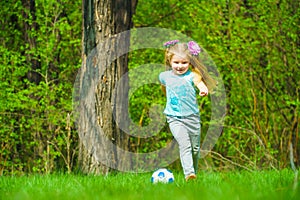 A cute little girl plays with a ball on a green meadow.