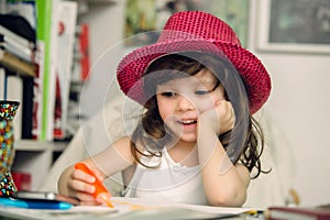 A cute little girl plays colouring at her desk. She is smiling and cheerful as she draws and colours.