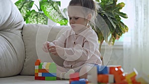 Cute little girl plays with plastic blocks puzzle at home.