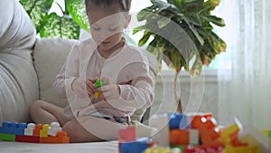 Cute little girl plays with plastic blocks puzzle at home.