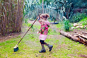 Cute little girl plays at sweeping the lawn