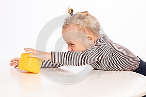 Cute little girl plays with an yellow block on a white background