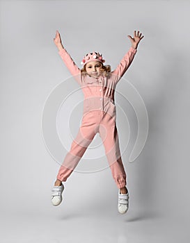 cute little girl with a plush crown jumps merrily with her hands up. in a cotton summer jumpsuit, dusty rose color, with