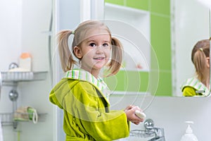 Cute child little girl with ponytail in green bathrobe washing her hands in bathroom