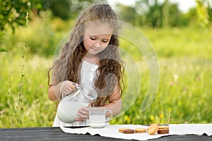 Cute little girl pouring milk in glass having breakfast outdoor summer