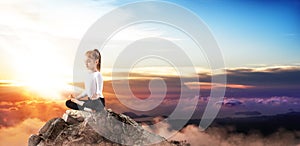 Cute little girl practice yoga on mountain peak cliff.