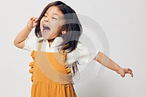 a cute little girl of preschool age is standing in an orange dress on a white background with her hands on her belt in