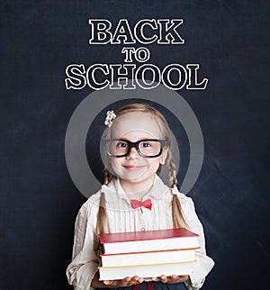 Cute little girl pupil holding pile of books and smiling