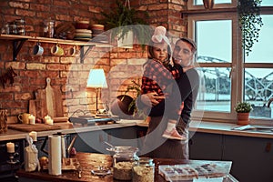 Cute little girl in rabbit makeup and hat sitting on hands of his father in loft style kitchen at morning.