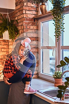 Cute little girl in rabbit makeup and hat sitting on hands of his father in loft style kitchen at morning.