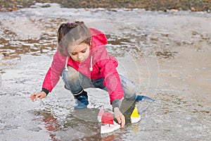 Cute little girl in rain boots playing with colorful ships in the spring creek standing in water