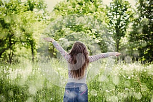Cute little girl with the raised hands in air standing against the magic nature in sunny day