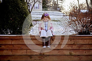 Cute little girl reading the Bible with an excited face in the winter park
