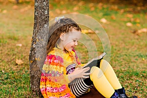 Cute little girl reading a book in autumn park