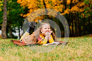 Cute little girl reading a book in autumn park