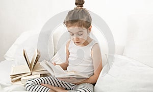 Cute little girl reading a book on the bed in the bedroom