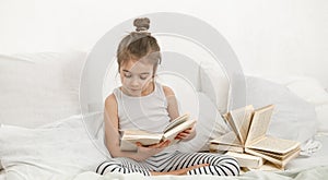 Cute little girl reading a book on the bed in the bedroom