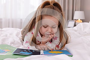 Cute little girl reading book on bed at home