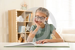 Cute little girl reading book at desk in room