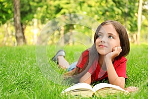 Cute little girl reading book on green grass in park