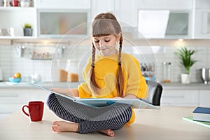 Cute little girl reading book in kitchen